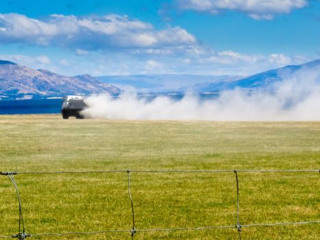 Truck spreading fertilizer on pasture meadow creating an enormous white dust cloud of rock phosphate and potash