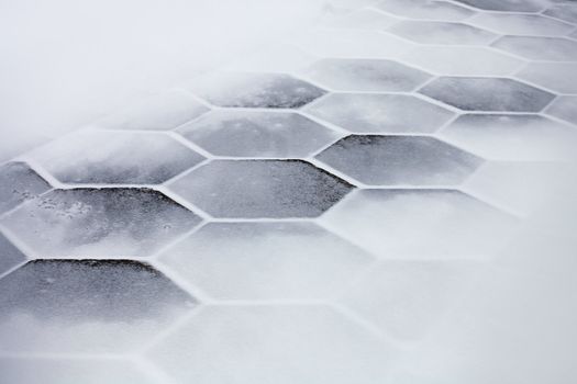 Hexagonal sidewalk tiles covered with snow and ice