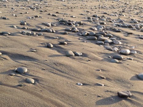 Background texture pattern of pebbles on a sandy water washed tidal beach in evening light