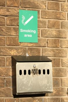 Designated smoking area. Metal ashtray outside on a bricked building's wall.