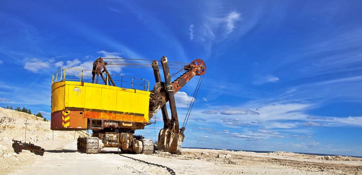 Heavy excavator in quarry for the extraction of gravel. Against the background of blue sky.