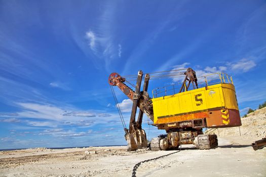 Heavy excavator in quarry for the extraction of gravel. Against the background of blue sky.