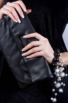 Beautiful female hands with manicure hold a black handbag