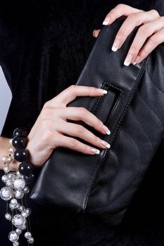 Beautiful female hands with manicure hold a black handbag