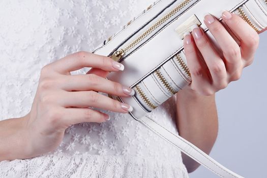 Beautiful female hands with manicure open a white handbag