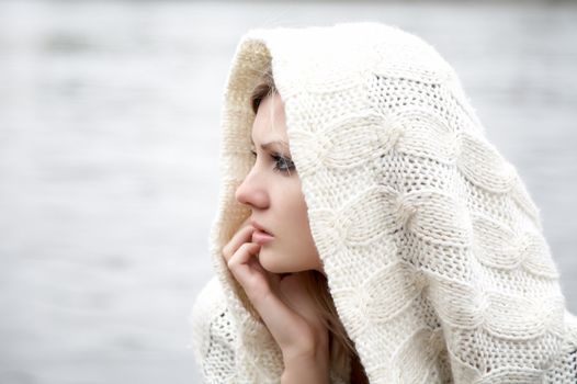 The thoughtful girl in  knitted dress on a background of water