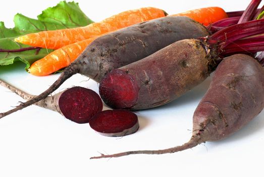 bunch of raw beet and carrot roots over white background
