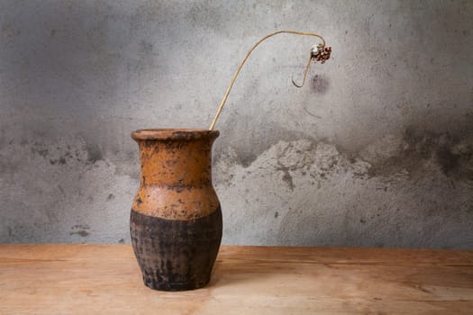 Still-life with an old jug and  dry plant on a wooden table