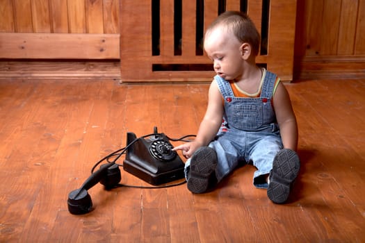 The little boy plays old phone sitting on a floor