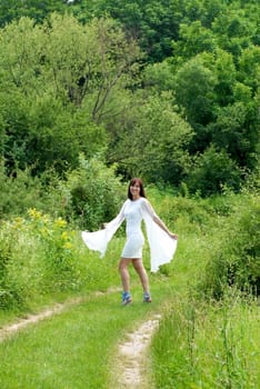 young happy caucasian brunette woman in white dress walking on green rural road