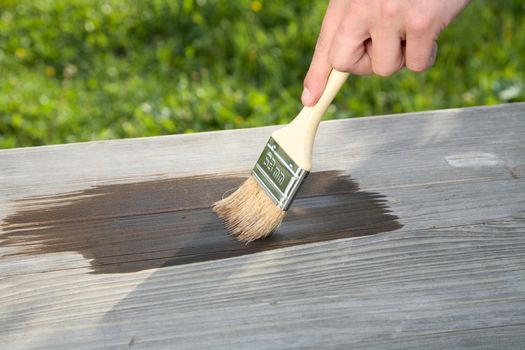  man's hand with  brush paints a board against green grass