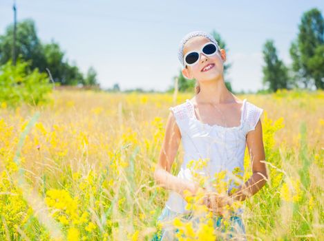 Adorable girl in glasses with flowers in yellow field. Summer freedom andjoy concept.