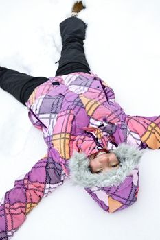 Happy teenage girl making snow angel in winter