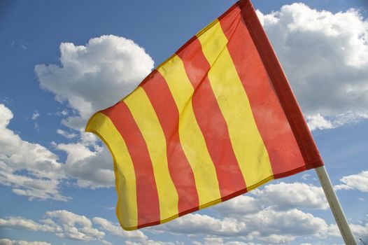 The orange striped flag on a background of the dark blue sky with clouds is yellow.
