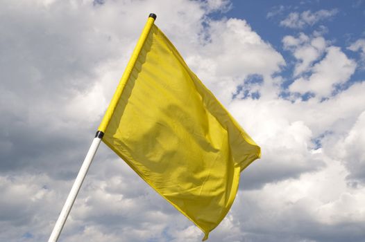 Yellow flag on a background of the dark blue sky with clouds.