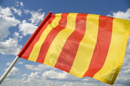 Yellow flag on a background of the dark blue sky with clouds.