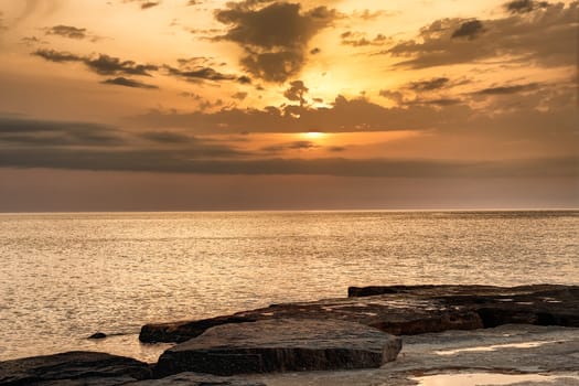 Evening sun going behind thin clouds as it set over the water glowing on the rocky shoreline