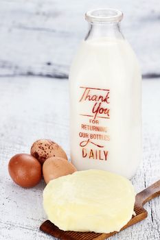 Farm fresh milk, butter, and eggs against a rustic background. Milk is in a vintage glass milk bottle. Shallow depth of field. 