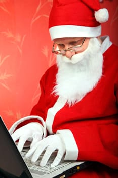 santa claus compose message on laptop computer. on the red wall background