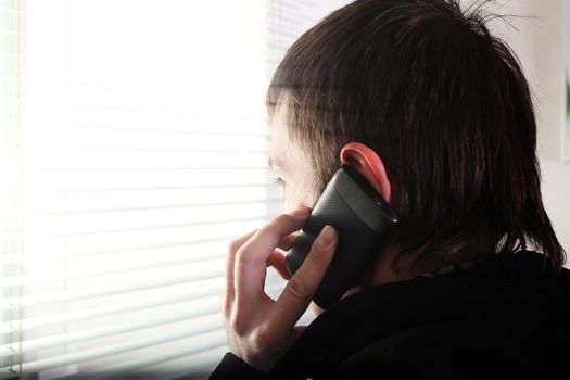 young man see through the jalousie and talking on mobile phone