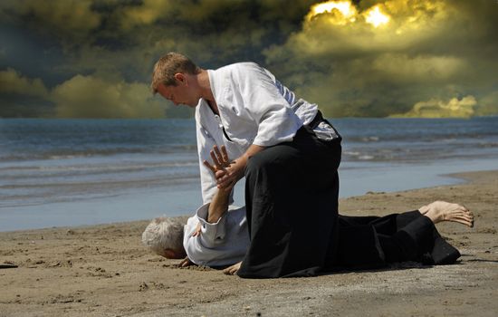 Two adults are training in Aikido on the beach