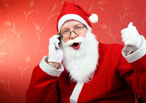 happy santa claus talking on mobile phone and show okay gesture. on the red wall background