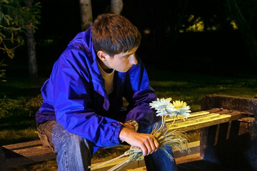 Sad Teenager in the Night Park with Flowers