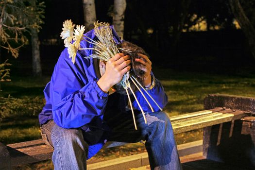 Troubled Teenager with a flowers and hidden face sitting in the night park