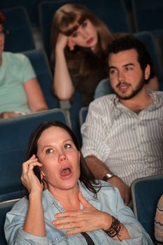 Woman talking on phone in theater with annoyed audience
