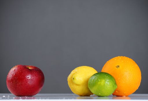 Different or standing out concept: one single red apple on one side with orange, lemon and lime together on the other, beautiful studio shot of wet fruits.