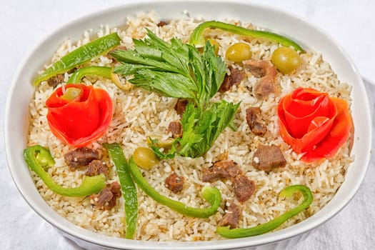 Rice with meat, olives, pepper and seasonings garnished with pealed tomato shaped like a flower.