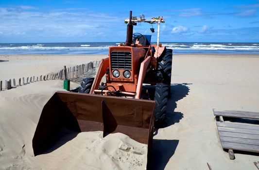 old red rusty tractor on the beach close to sea