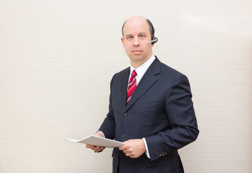 Business man with a handsfree telephone headset holding a document.