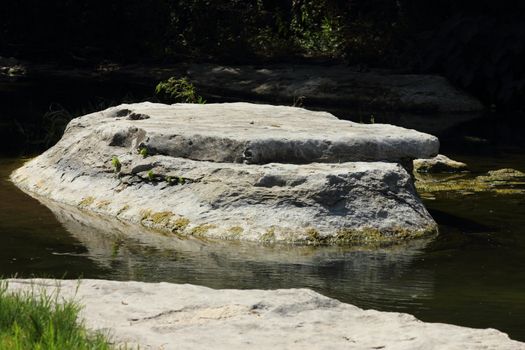 A large boulder sitting in the middle of a shallow pond.