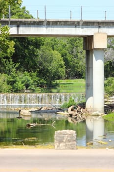 Bridge over man made waterfall with concrete wall.