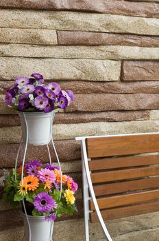 Colorful flowers in white pot wood chair and stone wall