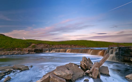 Waterfall of Tosna river riffle with quarry spalls in sunset light 
