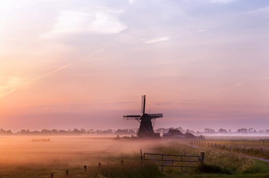 old Dutch windmill in fog in early morning during sunrise