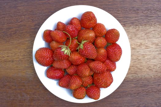 Red, ripe wild strawberry in a white plate on a brown background.