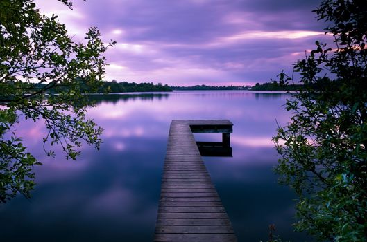 long wooden pier on lake at colorful sunset