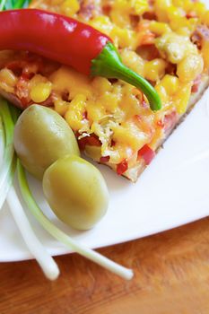 Piece of pizza with chili pepper and olives on plate