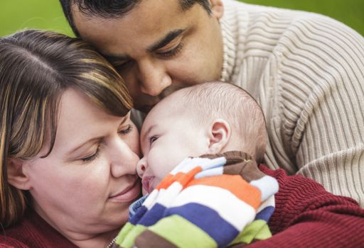 Happy Mixed Race Parents Hugging Their Son in the Park.