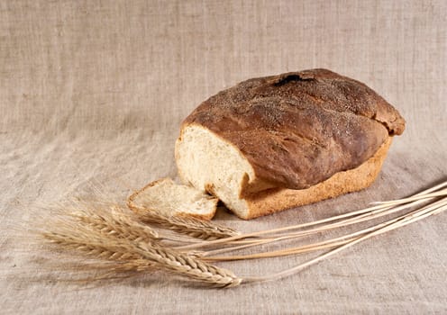 Loaf and slice of white wheat bread with wheatears on canvas