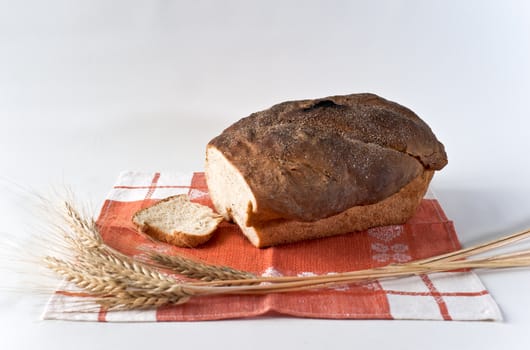 Loaf and slice of white wheat bread with wheatears on the red table-napkin