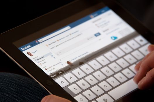 Stuttgart, Germany - January 29, 2012: Close up of an Apple iPad screen showing the Facebook website with two male hands typing a status update