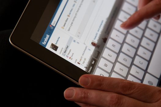 Stuttgart, Germany - January 29, 2012: Close up of an Apple iPad screen showing the Facebook website with female hands typing a status update