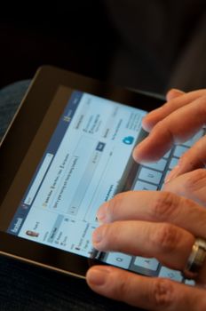 Stuttgart, Germany - January 29, 2012: Close up of an Apple iPad screen showing the Facebook website with two male hands typing a status update