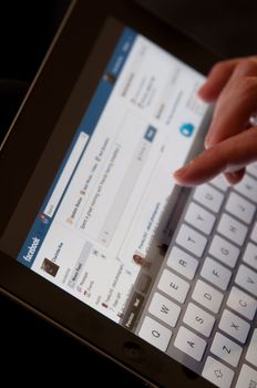 Stuttgart, Germany - January 29, 2012: Close up of an Apple iPad screen showing the Facebook website with female hands typing a status update