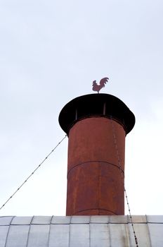 Grunge rusty metal tin chimney with rooster weather vane weathercock on top.