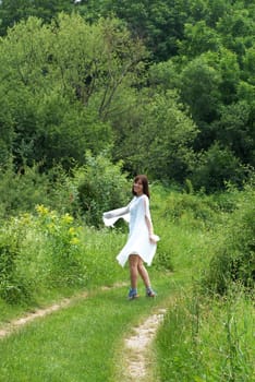 young happy caucasian brunette woman in white dress walking on green rural road